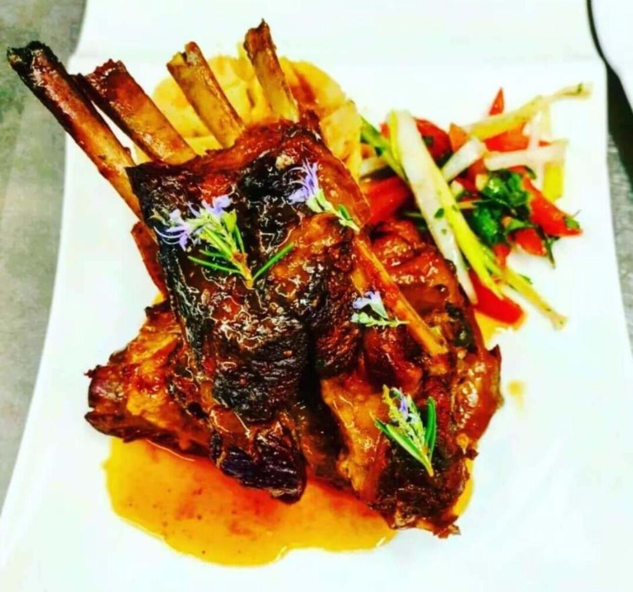 A plate of roasted lamb chops with a side of vegetables.
