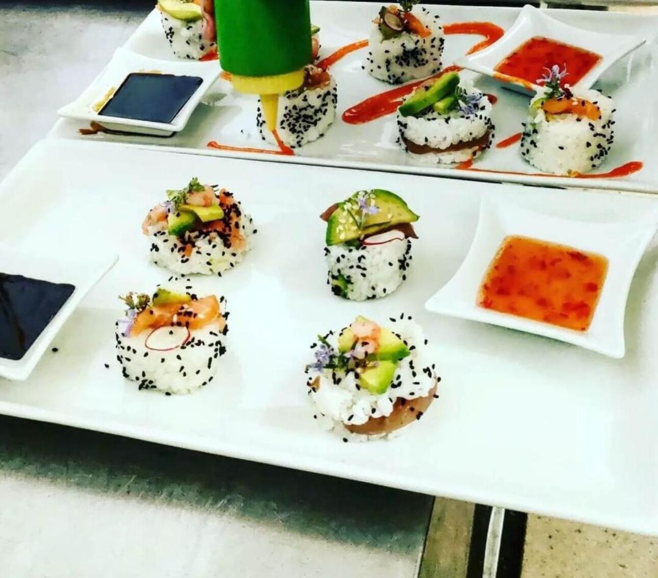 Una mesa blanca con diferentes platos de sushi y pequeños recipientes de salsa.