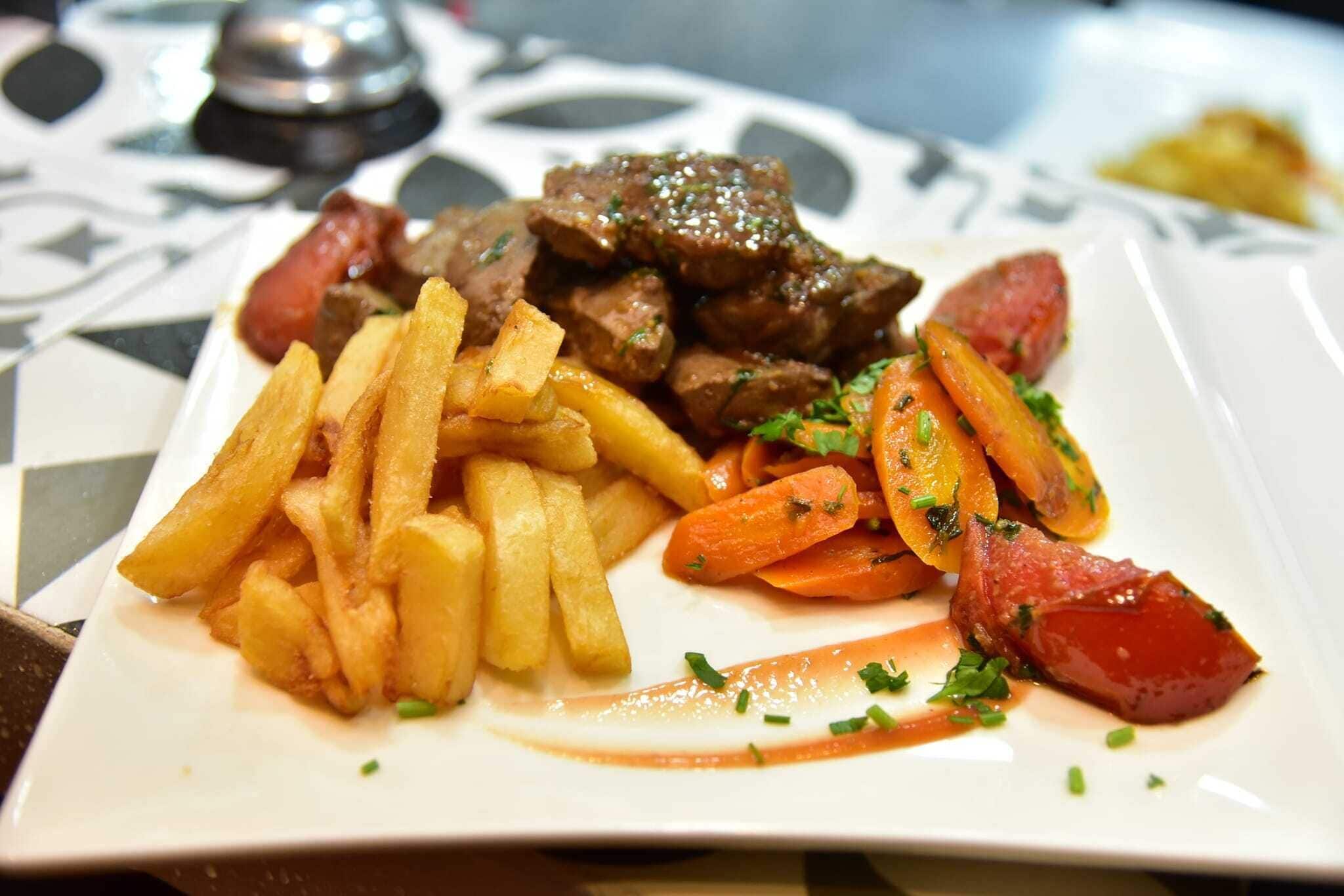 Un plato de comida con papas fritas, zanahorias y carne.