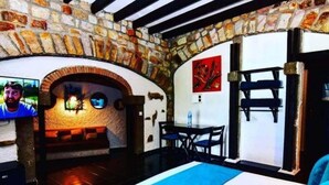 A cozy room with a stone wall, a fireplace, a bed, and a table with chairs. - Auberge Thais (Toudja)