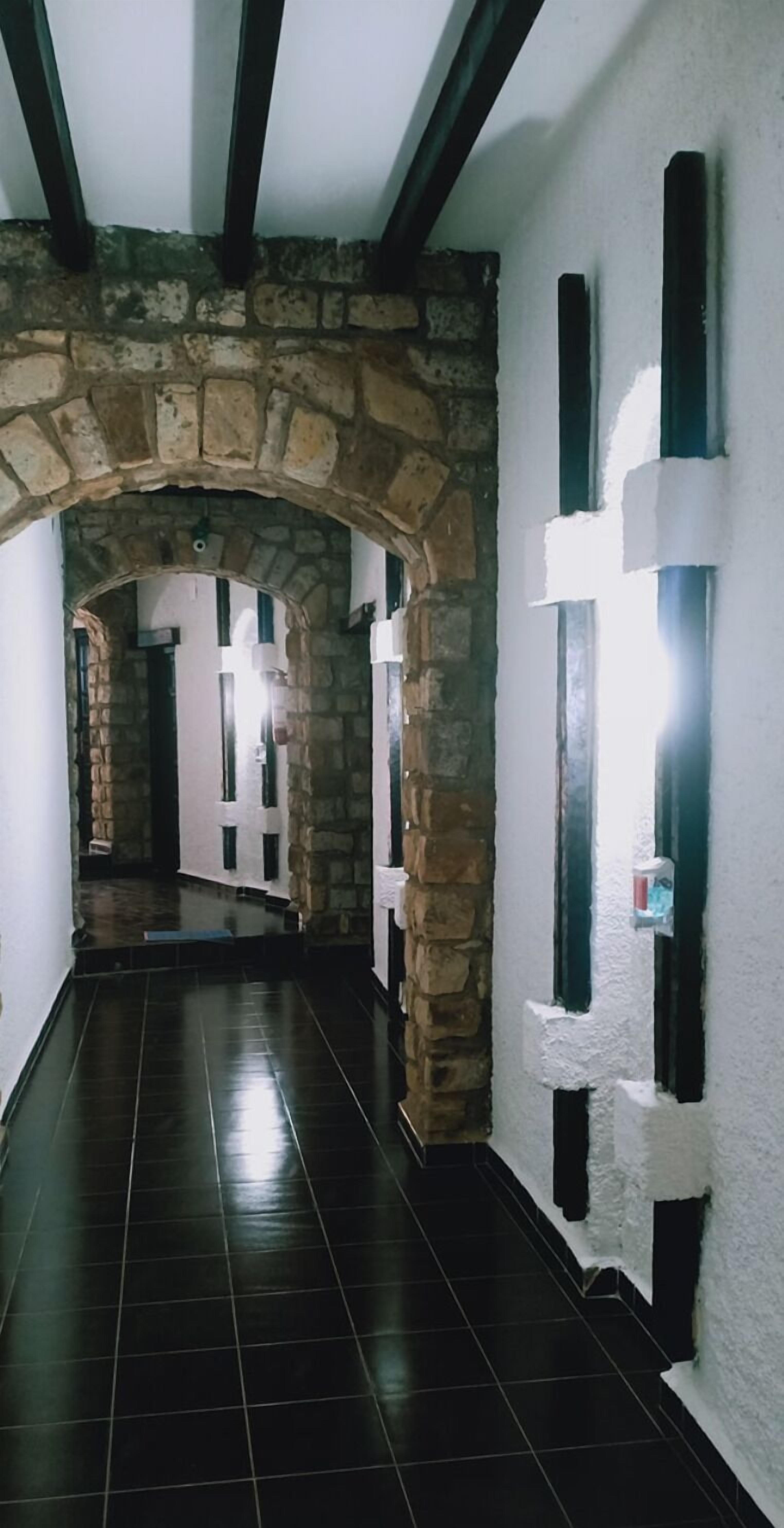 Un passadís amb arcs de pedra, paviment de rajoles i parets blanques amb detalls negres.
