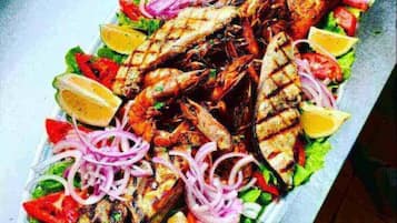 A platter of grilled fish with lemon slices, tomatoes, and red onions.