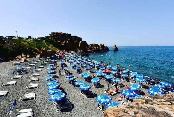 Privat strand, svart sandstrand, solstolar och parasoller