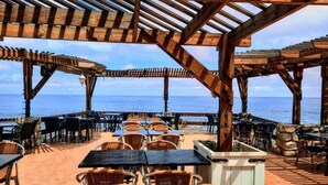 An outdoor dining area with tables and chairs, a pergola structure, and a view of the sea. - Auberge Thais (Toudja)
