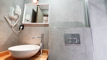 Un baño moderno con un lavabo blanco, un espejo, un secador de pelo de mano y una zona de ducha.
