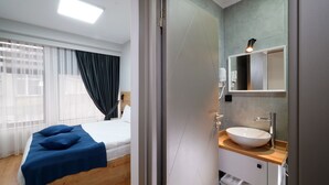 A modern hotel room with a bed, a large window with sheer curtains, a wooden floor, a bathroom with a large mirror, a sink, and a towel rack. - MEET ISTANBUL (Istanbul)