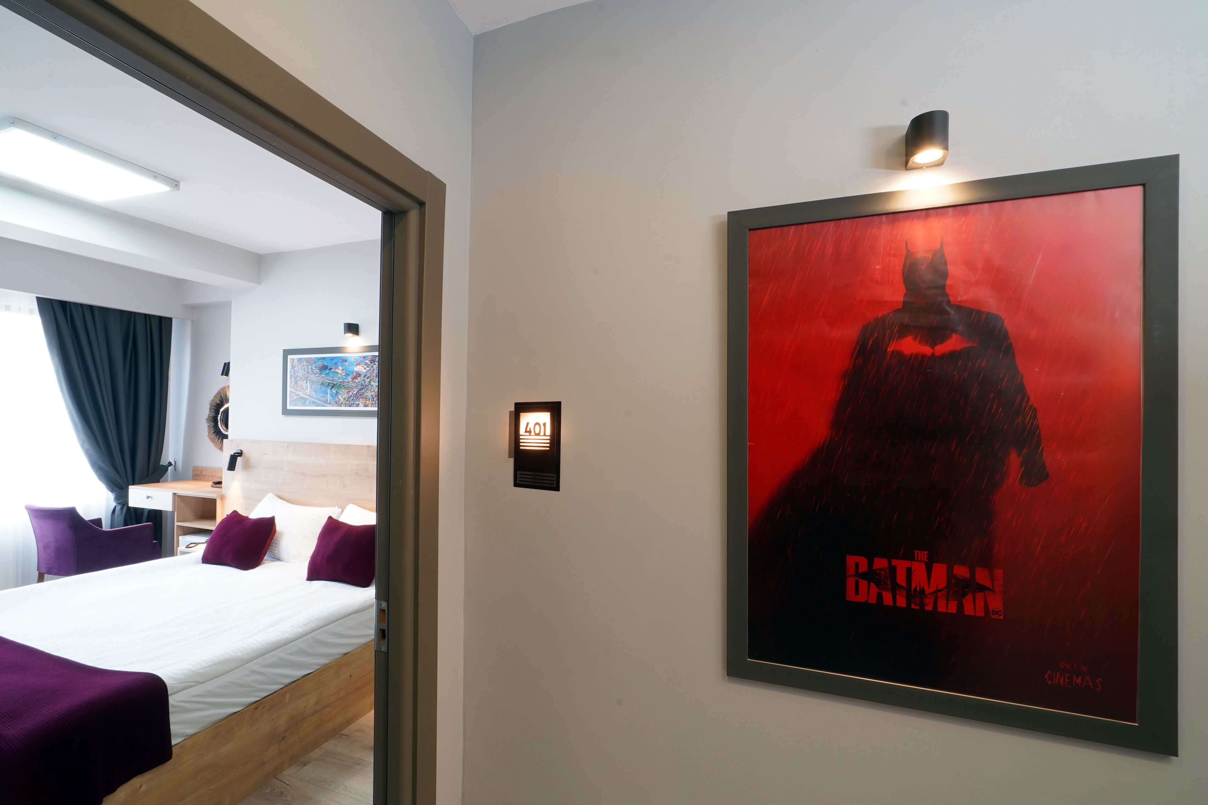 Une chambre d’hôtel avec un lit, un bureau et une affiche de Batman accrochée au mur.