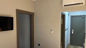 A hotel room with a bed, a mounted TV, an air conditioning unit, a door, and a hallway with a wooden floor. - MEET ISTANBUL (Istanbul)