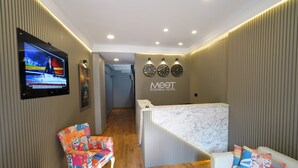 A hotel reception area with a marble counter, a television displaying a news channel, and a colorful chair. - MEET ISTANBUL (Istanbul)