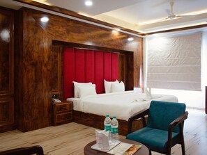 A hotel room with a wooden headboard, a large bed, a bedside table with a phone, a chair, and a table with water bottles and a menu.