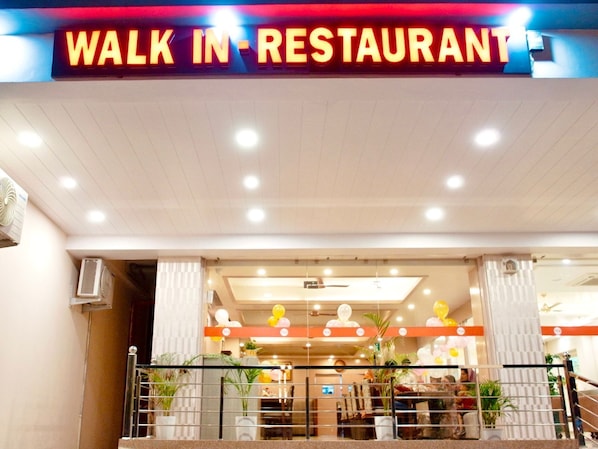 A restaurant with a 'WALK IN RESTAURANT' sign, indoor lighting, and a balcony with plants.