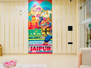 A vibrant mural of Jaipur's heritage, a modern elevator, and a glimpse of the room's interior.