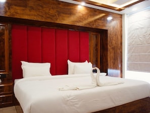 A hotel room with a large bed, red headboard, wooden paneling, and a white bedspread.