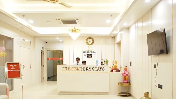 A reception area at The Century Stays hotel with a reception desk, a clock, and a television mounted on the wall. -  The Century Stays (Jaipur)