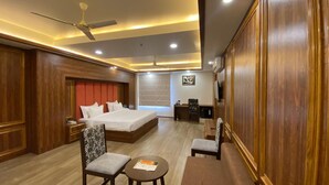 A hotel room with a large bed, a desk, a chair, a small table, and a ceiling fan. -  The Century Stays (Jaipur)