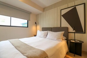 Quarto de hotel moderno com uma cama grande, mesa de cabeceira, luminária na parede e janela com persianas.