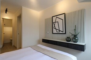 A modern bedroom with a bed, a wall-mounted shelf with vases, and a geometric artwork.