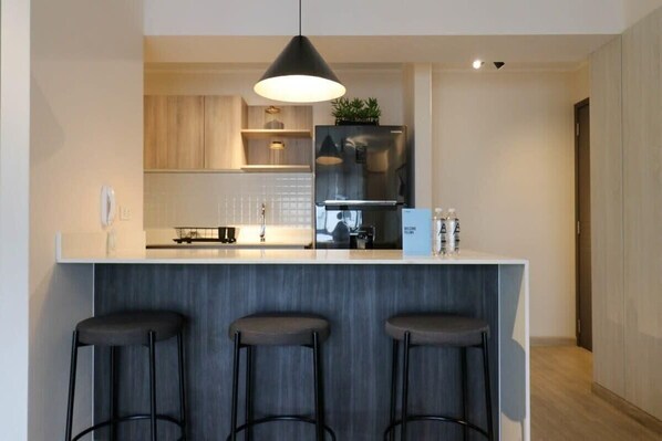 A modern kitchen with a central island, bar stools, a hanging light fixture, and a built-in refrigerator.