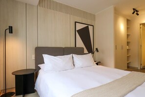 Ein modernes Hotelzimmer mit einem großen Bett, einem Nachttisch, einer Stehlampe und einem Kleiderschrank.
