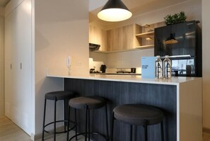A modern kitchen with a white countertop, black stools, and a black refrigerator.