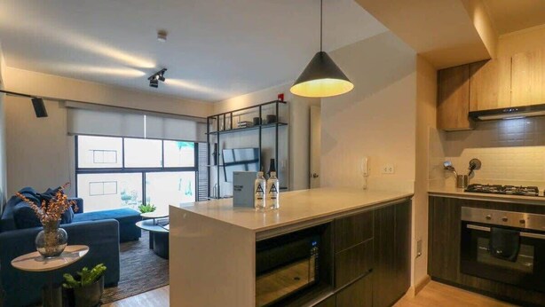 A modern kitchen with a central island, built-in appliances, and a dining area with a sofa and coffee table. - w* | Perfect 1BR w/ Great Deco in Barranco (Barranco)
