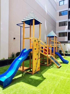 A children's play structure with slides and climbing areas, set against a building facade.