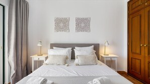 Un lit bien fait, avec du linge de lit blanc, deux tables de chevet avec des lampes et une armoire en bois.