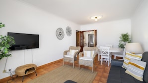 Un salon équipé d’un téléviseur à écran plat, de fauteuils en osier, d’un canapé, d’une table à manger avec des chaises et d’un petit tapis.