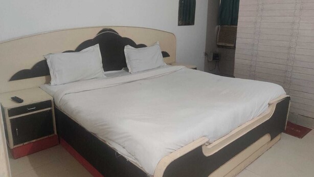 A single bed with a headboard, a nightstand, and a wall-mounted air conditioning unit. - Hotel Abhishek Residency By The Arrow (New Delhi)