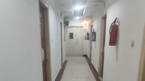 A long, narrow hallway with white walls and a tiled floor. There are fire extinguishers mounted on the walls and a door at the end of the hallway. - Hotel Abhishek Residency By The Arrow (New Delhi)