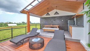 A modern outdoor deck with lounge chairs, a round table, and a kitchen area. - Villa Dharman B7 (Ubud)