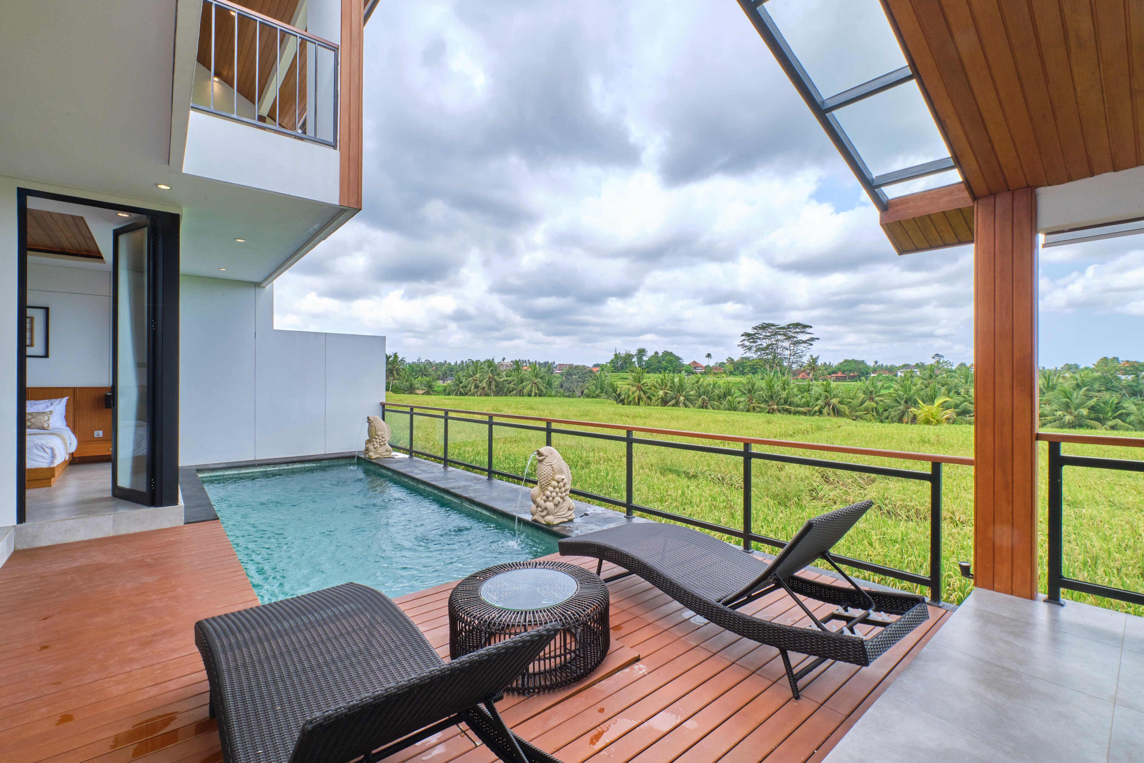 A modern outdoor pool area with lounge chairs, a small table, and a view of a lush landscape.
