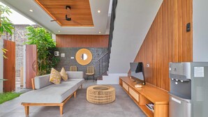 A modern living space with a sofa, ottoman, and wooden entertainment unit. - Villa Dharman B7 (Ubud)