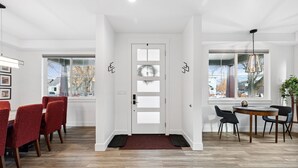 A modern interior with a wooden floor, a white door with frosted glass panels, and a dining area with red and black chairs.