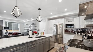 A modern kitchen with a large island, stainless steel appliances, and pendant lighting.