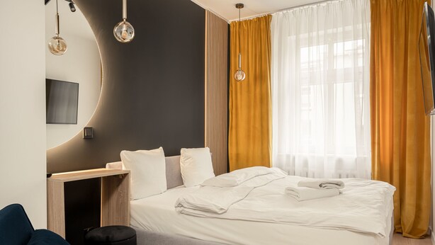 Et moderne hotelværelse med en pænt redt seng, et skrivebord med stol, et fladskærms-tv og et stort vindue med gardiner.