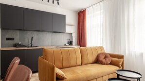 En moderne opholdsstue med sofa, to sofaborde, et tekøkken og et vindue med gardiner.