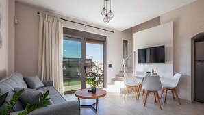 A modern living room with a sofa, a round table, and a TV mounted on the wall. - Modern facilities, walking distance to the beach! (Panormo)