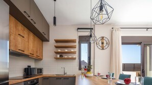 A modern kitchen with wooden cabinets, a microwave, and a stove. There is a dining area with a table, chairs, and a view of the outdoors. - Modern facilities, walking distance to the beach! (Panormo)