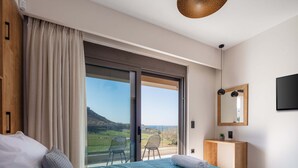 A bedroom with a large bed, a view of the outdoors, a wooden bedside table, and a mirror on the wall. - Modern facilities, walking distance to the beach! (Panormo)