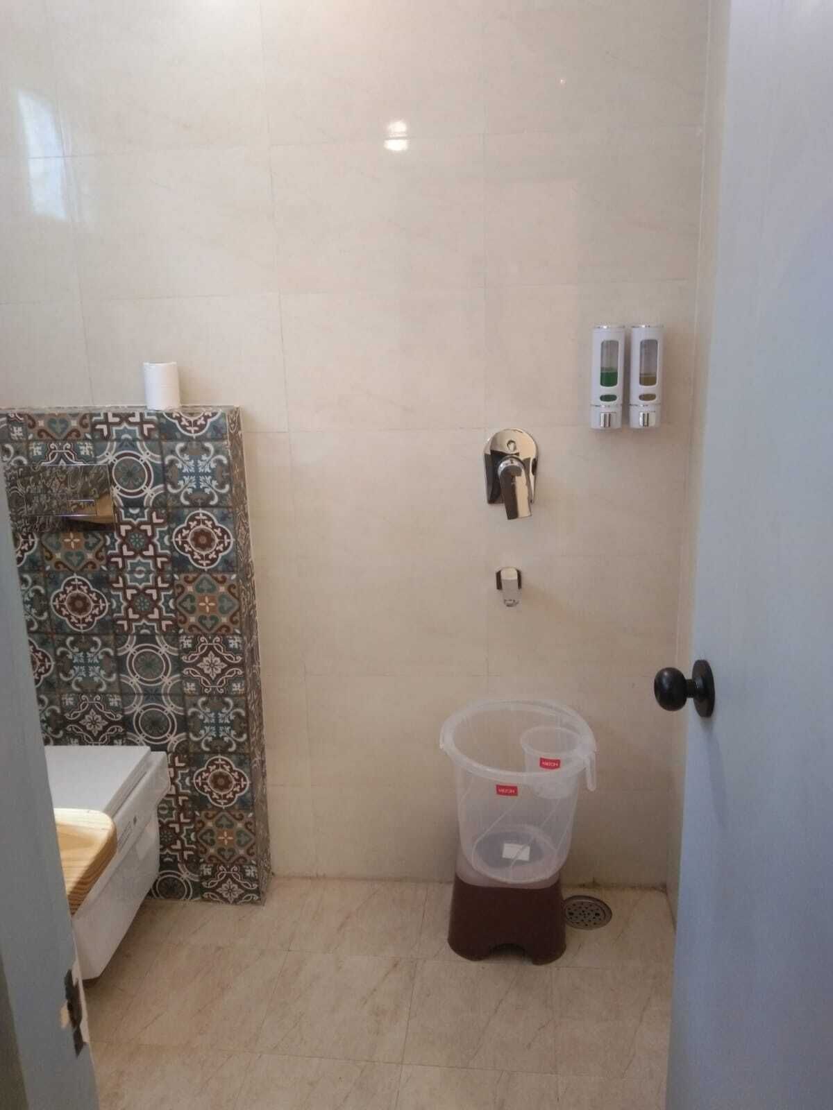 A small bathroom with a shower, a toilet, and a sink. There are two soap dispensers on the wall and a trash bin.