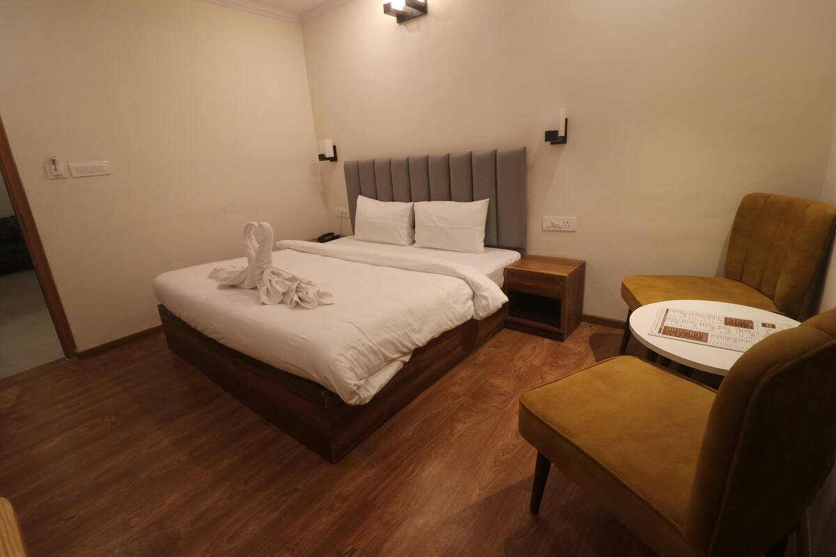A hotel room with a large bed, a bedside table, a chair, and a small table with a menu.