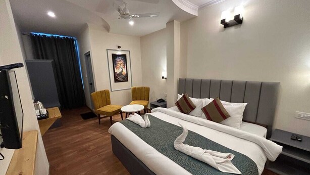 Habitación de hotel con cama, dos sillas, una mesita, un escritorio, un ventilador de techo y un cuadro en la pared.