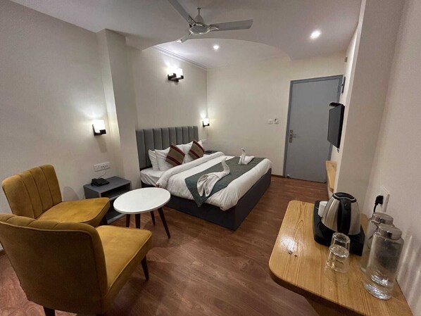 A hotel room with a bed, two armchairs, a small round table, a coffee maker, and a TV.