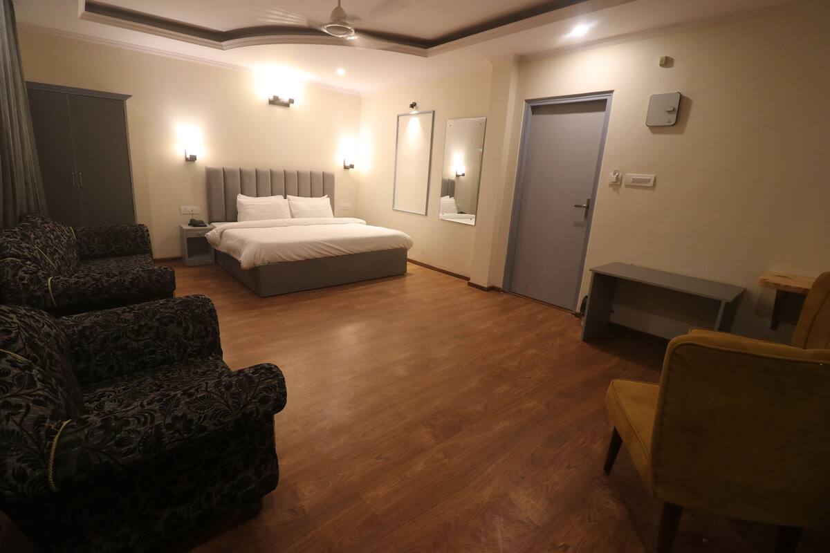 A hotel room with a bed, two armchairs, a bench, and a wardrobe.