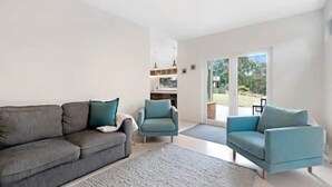 A modern living room with a grey sofa, two blue armchairs, and a large window offering a view of the outdoors. - Serenity at Ridgeway Retreat Relax Hike Bike (Ridgeway)