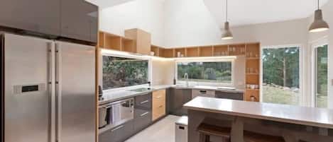 A modern kitchen with a large island, stainless steel appliances, and a view of the outdoors.