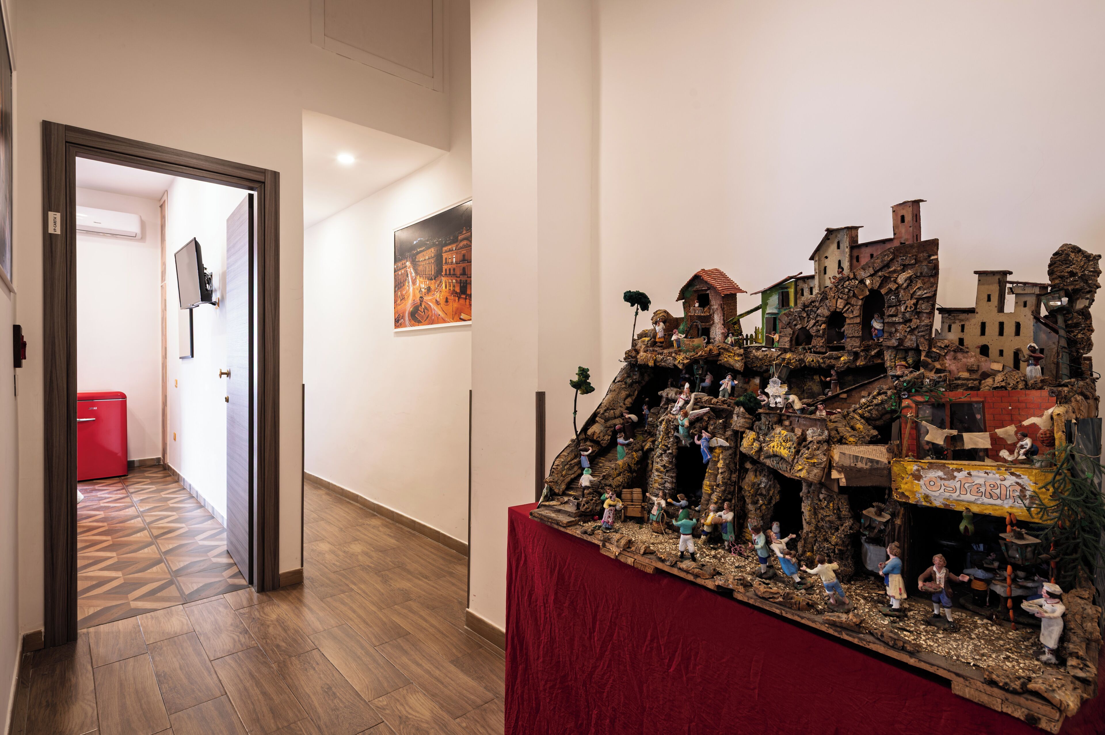 A hallway with a red suitcase, a wooden floor, and a model display on a table.