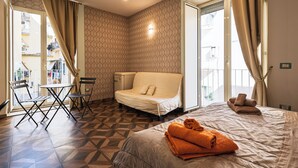 A hotel room with a bed, a sofa, a small table, and chairs. There is a window with curtains, a wall-mounted light, and a view of buildings outside. - PIGNASECCA GUEST HOUSE  (Naples)