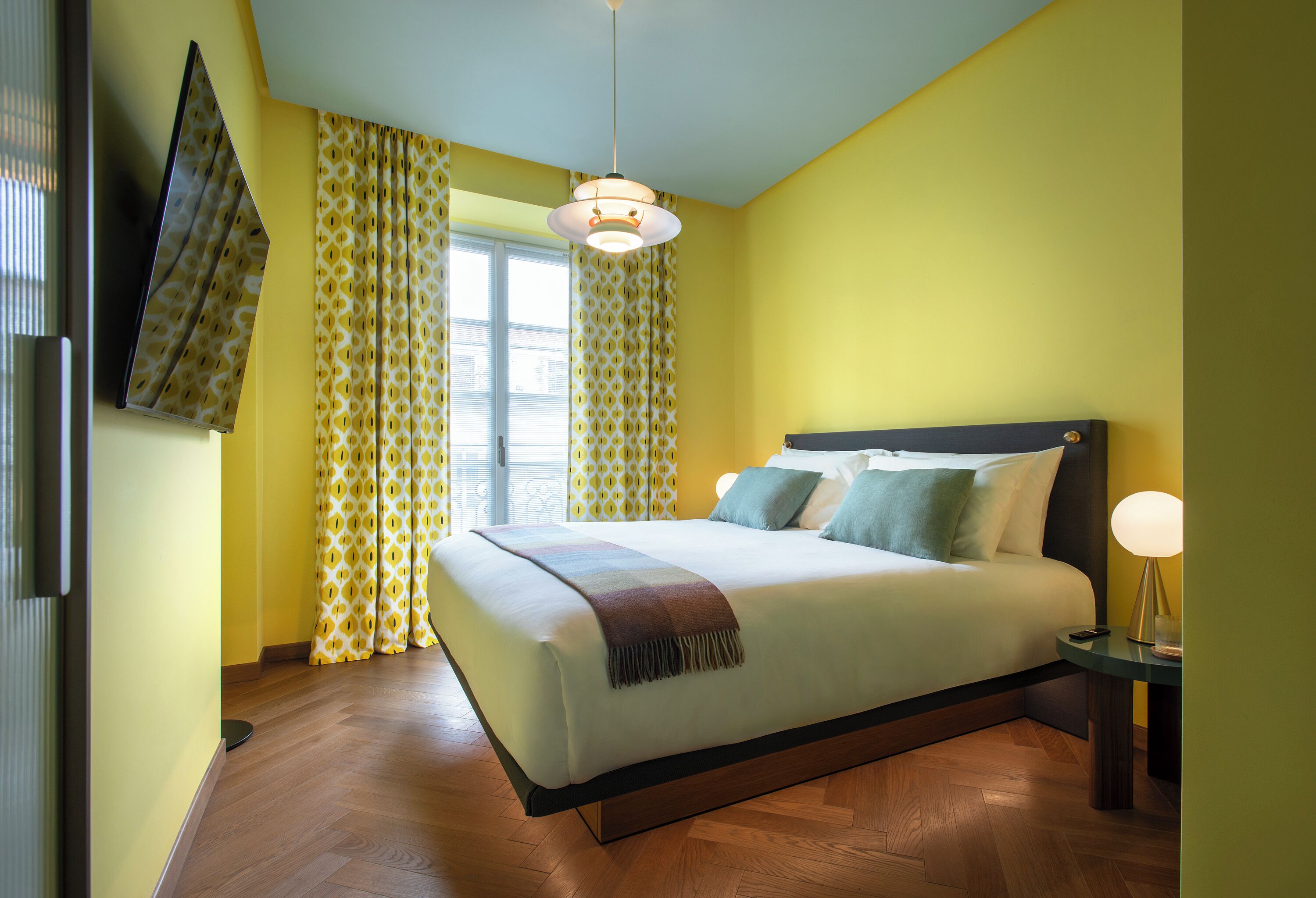 A bedroom with a bed, curtains, a hanging light fixture, and a bedside table.